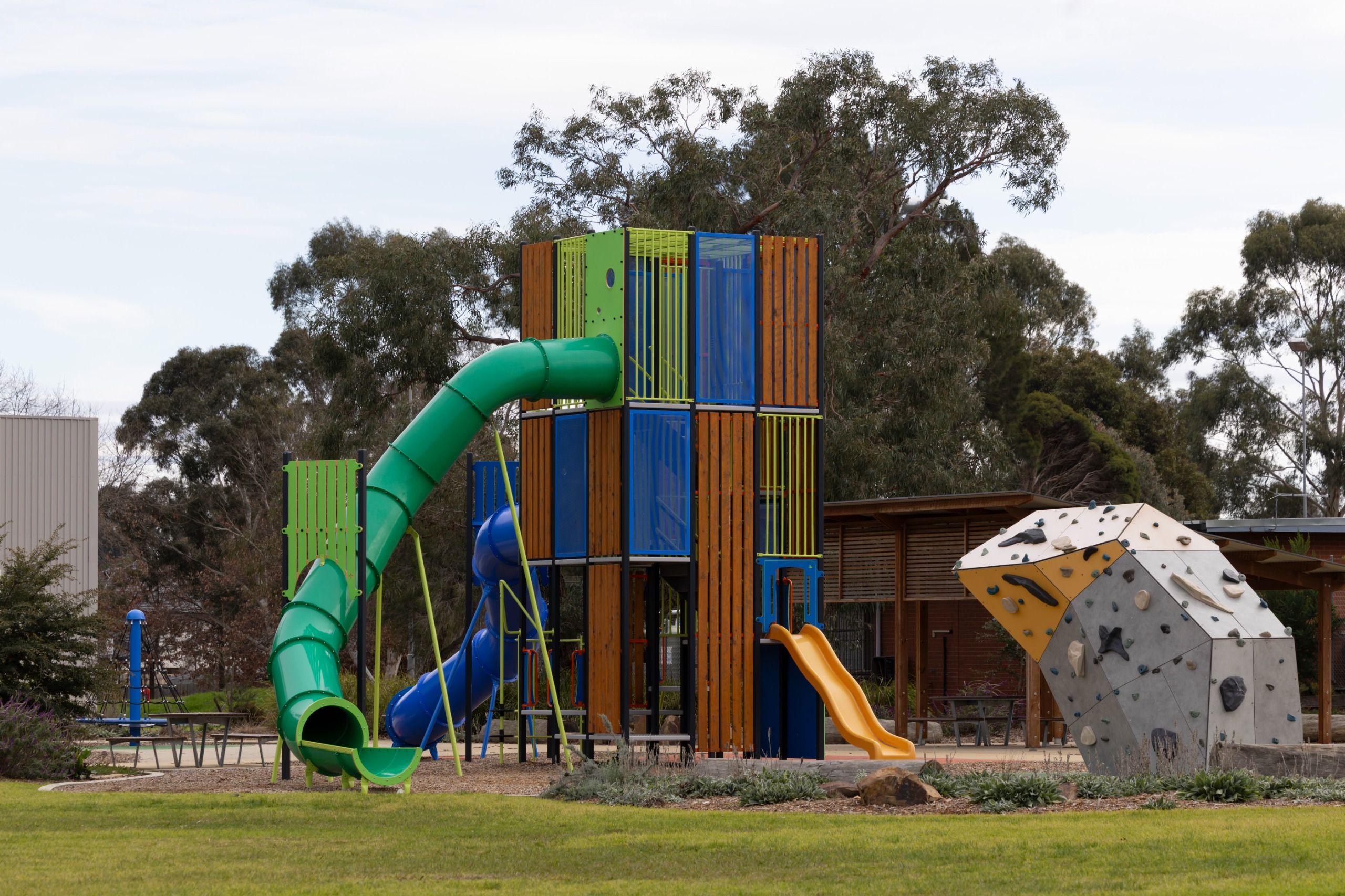 Kids playground with a large green slide, small yellow slide and a climbing rock
